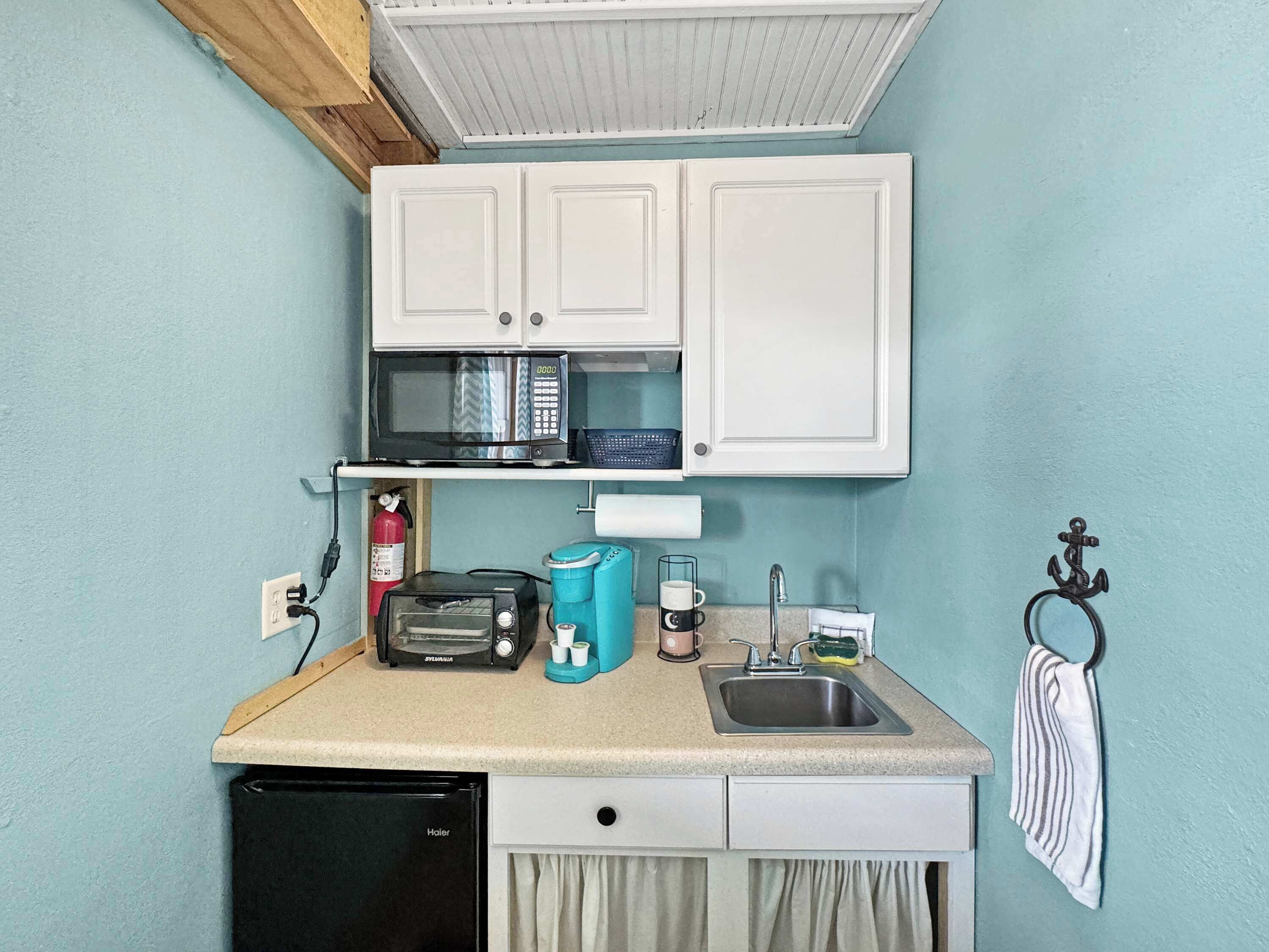 Una kitchenette compacta con microondas, tostadora, pileta y heladera pequeña.