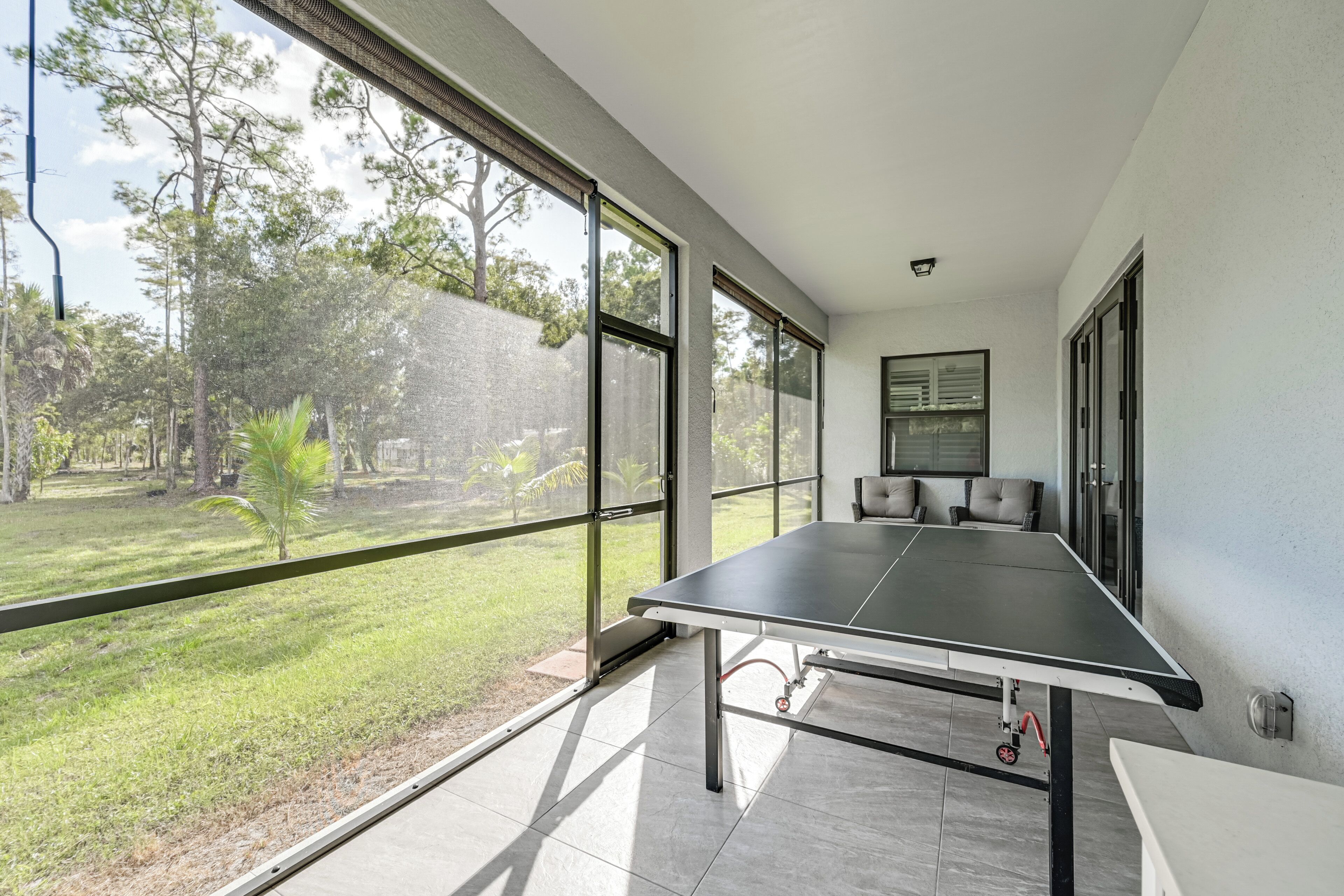 A spacious room with a ping pong table, large windows offering a view of a grassy area, and a modern interior design.