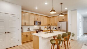A modern kitchen with wooden cabinets, a central island with bar stools, a microwave, and a refrigerator. - Great for Families! Newly Built Home in Aurora (Aurora)
