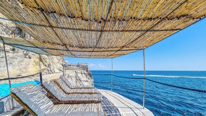 Eine Strandlounge mit Reetdach, gepolsterten Sitzgelegenheiten und Blick auf das Meer.
