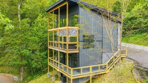Une cabane en bois à plusieurs niveaux, dotée d’un balcon et entourée d’une forêt dense.