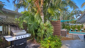 Un cortile con una griglia per barbecue, palme, una piscina e una recinzione in legno.
