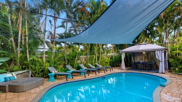 Una piscina con lettini e un'area ombreggiata, circondata da palme e vegetazione.