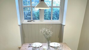 A dining table set with plates, cutlery, and a vase of flowers, positioned under a window with a view of trees. - Cosy cottage in the heart of Stow-on-the-Wold, pet-friendly (Stow-on-the-Wold)