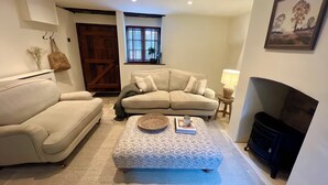 A cozy living room with a beige sofa, a matching ottoman, a small side table with a lamp, and a fireplace. - Cosy cottage in the heart of Stow-on-the-Wold, pet-friendly (Stow-on-the-Wold)