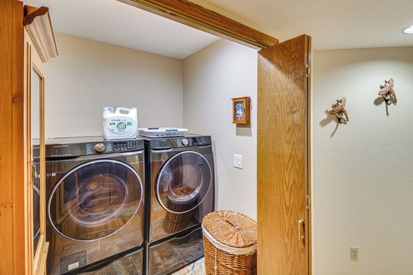 A laundry area with two stacked front-loading washers and dryers, a wicker basket, and a wall-mounted picture. - Large Family Duplex w/ Grill, Near Beaver Creek (Avon)