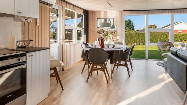 Et moderne køkken med træskabe, et spiseområde med bord og stole, og udsigt til haven gennem store vinduer.