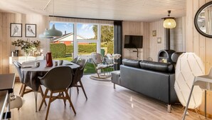 En moderne stue med en sort lædersofa, et spiseområde med et rundt bord, og et stort vindue med udsigt over det fri.