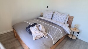 Una cama bien hecha con un edredón gris y estampado, un cabecero de madera y una mesita de noche con una lámpara.