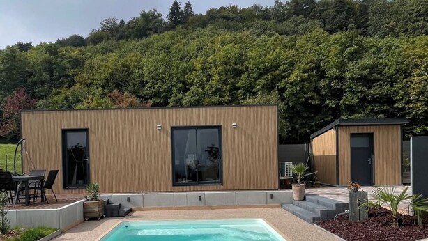 Un área de piscina moderna con una piscina rectangular, cubierta de madera y un pequeño rincón de descanso con sillas y una mesa.