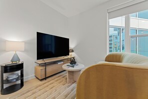 Une chambre d’hôtel moderne équipée d’une télévision à écran plat, d’une petite table ronde, d’un canapé et d’une grande fenêtre donnant sur la ville.