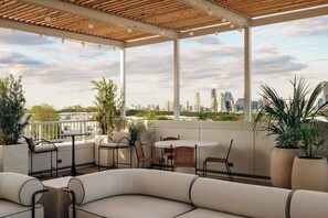 A covered outdoor seating area with a city skyline view, featuring a round table, chairs, and potted plants.