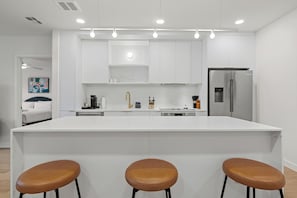 Una cocina moderna con armarios blancos, una isla central con taburetes y un refrigerador de acero inoxidable.
