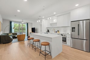 A modern kitchen with a central island, bar stools, stainless steel appliances, and a dining area with a sofa and coffee table.