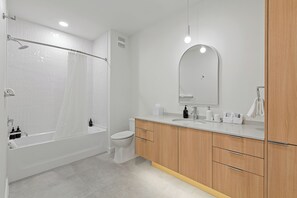 A modern bathroom with a bathtub, toilet, vanity with mirror, and wooden cabinets. - Experience Zilker & South Lamar from The Code | Private Balcony w/ Pool, Bar (Austin)