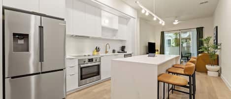 A modern kitchen with stainless steel appliances, a central island with bar stools, and a view of the outdoors.