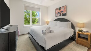 A modern bedroom with a bed, bedside table, nightstand, window, and ceiling fan. - Experience Zilker + South Lamer | Private Balcony | Pool, Dining, Bar | The Code (Austin)