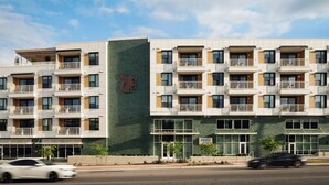 A multi-story hotel with balconies, a prominent logo on the facade, and a sign indicating a restaurant. - Experience Zilker + South Lamer | Private Balcony | Pool, Dining, Bar | The Code (Austin)