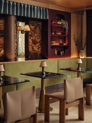 A restaurant with booths, tables, and a wall with a floral tapestry and shelves.