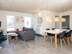 Una sala moderna con un sofá gris, una mesa de comedor con sillas negras y un ventanal grande.