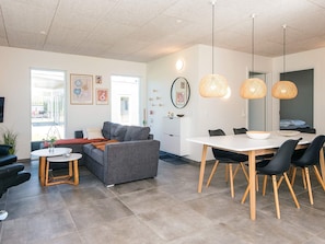 Una sala de estar moderna con un sofá gris, una mesa de centro redonda y una zona de comedor con una mesa blanca y sillas negras.