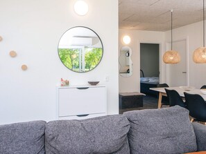 A modern living room with a grey sofa, a round mirror, and a dining area with a table and chairs.