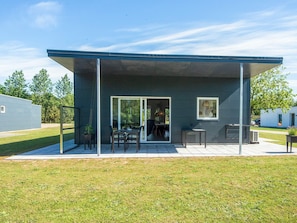 Un edificio moderno con un patio cubierto, grandes puertas de cristal y una pequeña mesa con sillas.