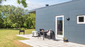A modern building with a grey exterior, a door, a window, and a patio area with a table and chairs.