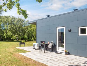 A modern building with a grey exterior, a door, a window, and a patio area with a table and chairs.