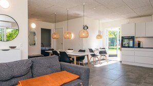 A modern living room with a grey sofa, a white coffee table with a vase, and a dining area with a white table and chairs.