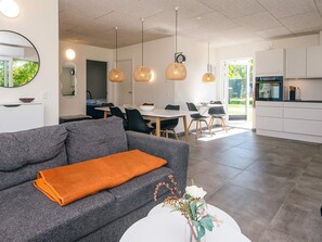 A modern living room with a grey sofa, a white coffee table with a vase, and a dining area with a white table and chairs.