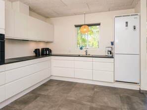 A modern kitchen with white cabinets, a black countertop, a built-in oven, a coffee maker, and a window with a view of trees.