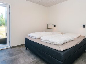 A bedroom with a bed, a door, and a wall-mounted shelf.