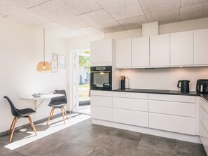 A modern kitchen with white cabinets, a black countertop, and a dining area with two chairs.