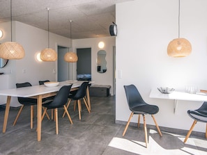 Un espace de salle à manger moderne avec une table blanche, des chaises noires et des suspensions en fibres tressées.