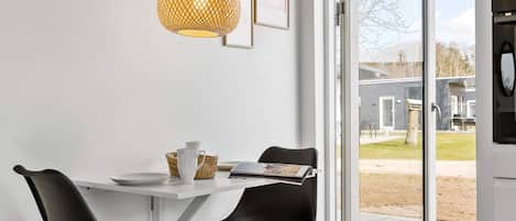 A modern kitchen with a white countertop, two black chairs, a hanging pendant light, and a glass door leading outside.
