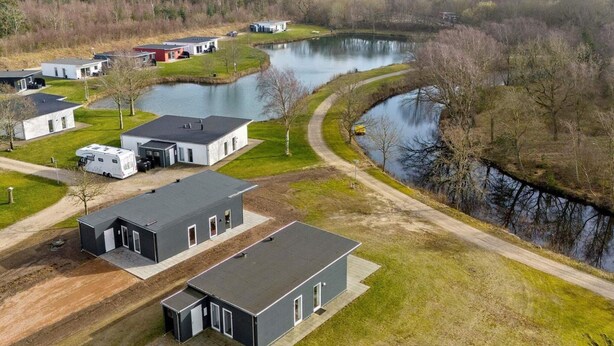 A modern residential area with multiple houses, a small lake, and a dirt road.