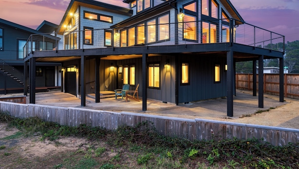 Une maison moderne à plusieurs étages, dotée d’un patio couvert, de grandes fenêtres et d’une terrasse en bois.