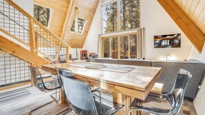 A modern loft-style interior with a wooden dining table, clear chairs, a sofa, and a TV mounted on the wall. - Sleeps 20, 2 Homes Near Ski Resort | Beach + Lake Access, Pool | Homewood (Tahoma)