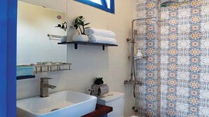 A bathroom with a white sink, a toilet, a shelf with towels, and a shower with patterned tiles. - SEA FLOWER HOUSE (Thanh pho Hoi An)