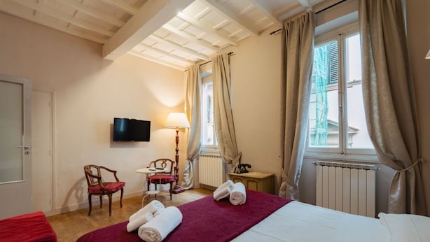 Une chambre d’hôtel avec un lit, une télévision, une chaise, une table et une fenêtre avec des rideaux.