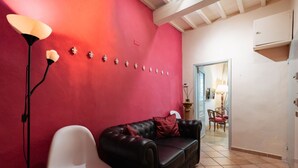 Une pièce avec un mur rouge, un canapé en cuir noir, une chaise blanche, un lampadaire et, au fond, un coin repas.
