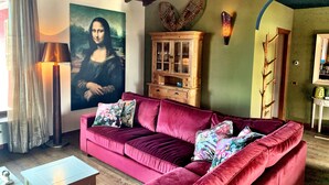 A living room with a red velvet sofa, a wooden cabinet, a painting of the Mona Lisa, and a ladder against the wall.