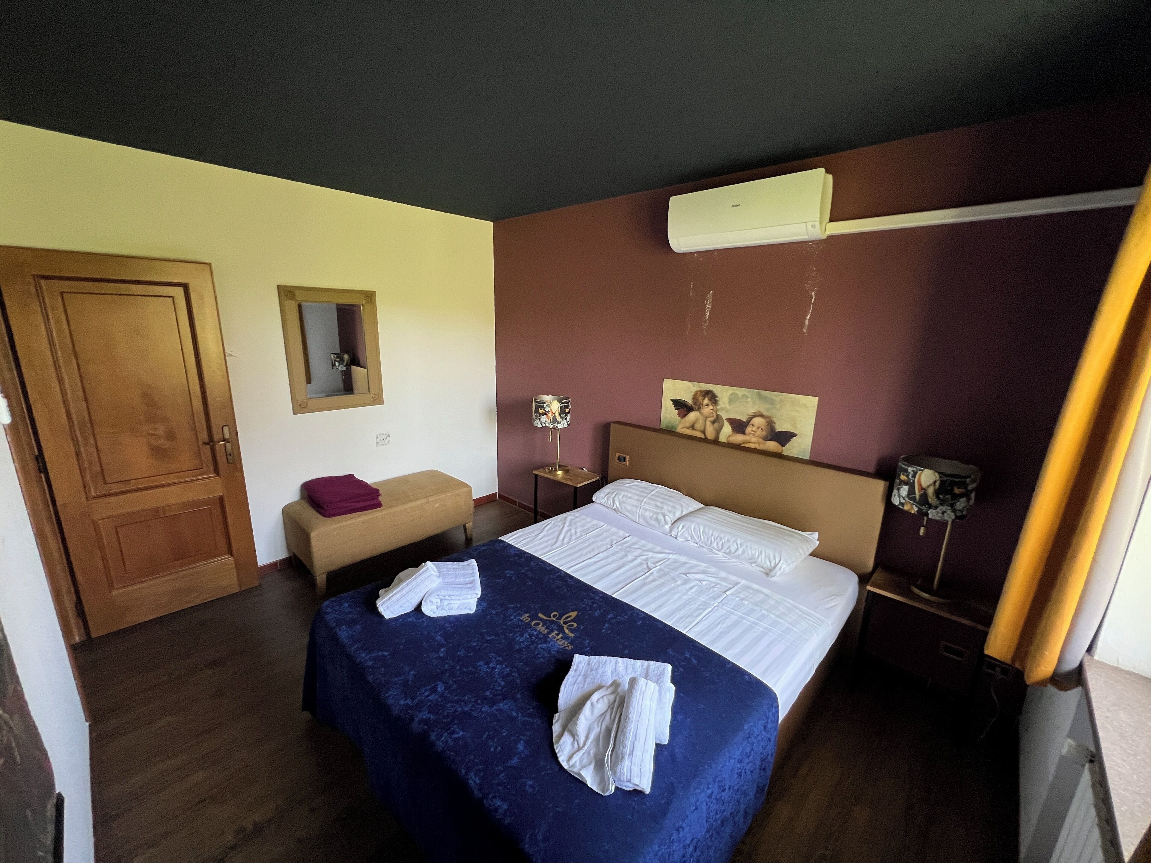 Ein Hotelzimmer mit Bett, Sitzbank, Spiegel, einem Gemälde und einer Klimaanlage.