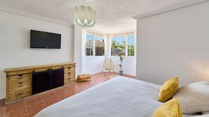 Una camera da letto con un letto, una televisione, un armadio in legno, una sedia e una finestra con vista su edifici e alberi.