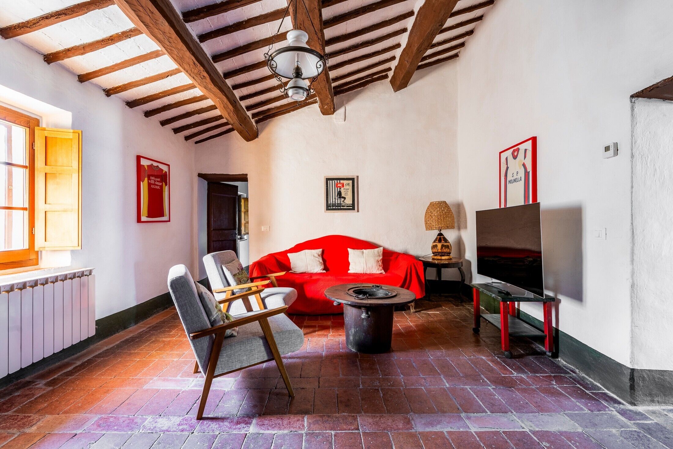 A room with a red sofa, a wooden chair, a TV on a stand, a lamp, and a fireplace.