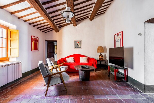 A room with a red sofa, a wooden chair, a TV on a stand, a lamp, and a fireplace.