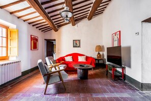 A room with a red sofa, a wooden chair, a TV on a stand, a lamp, and a fireplace.
