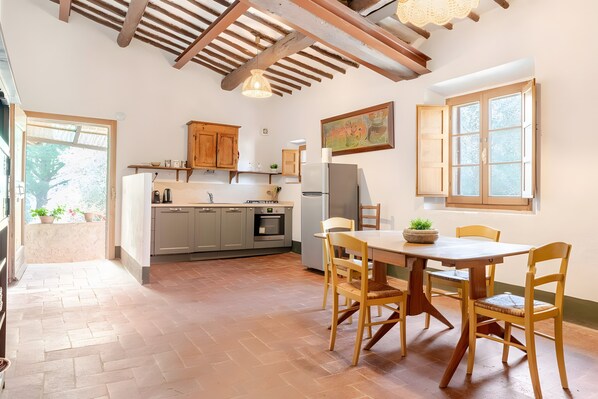 A kitchen with wooden cabinets, a dining table with chairs, and a window with a view of trees.
