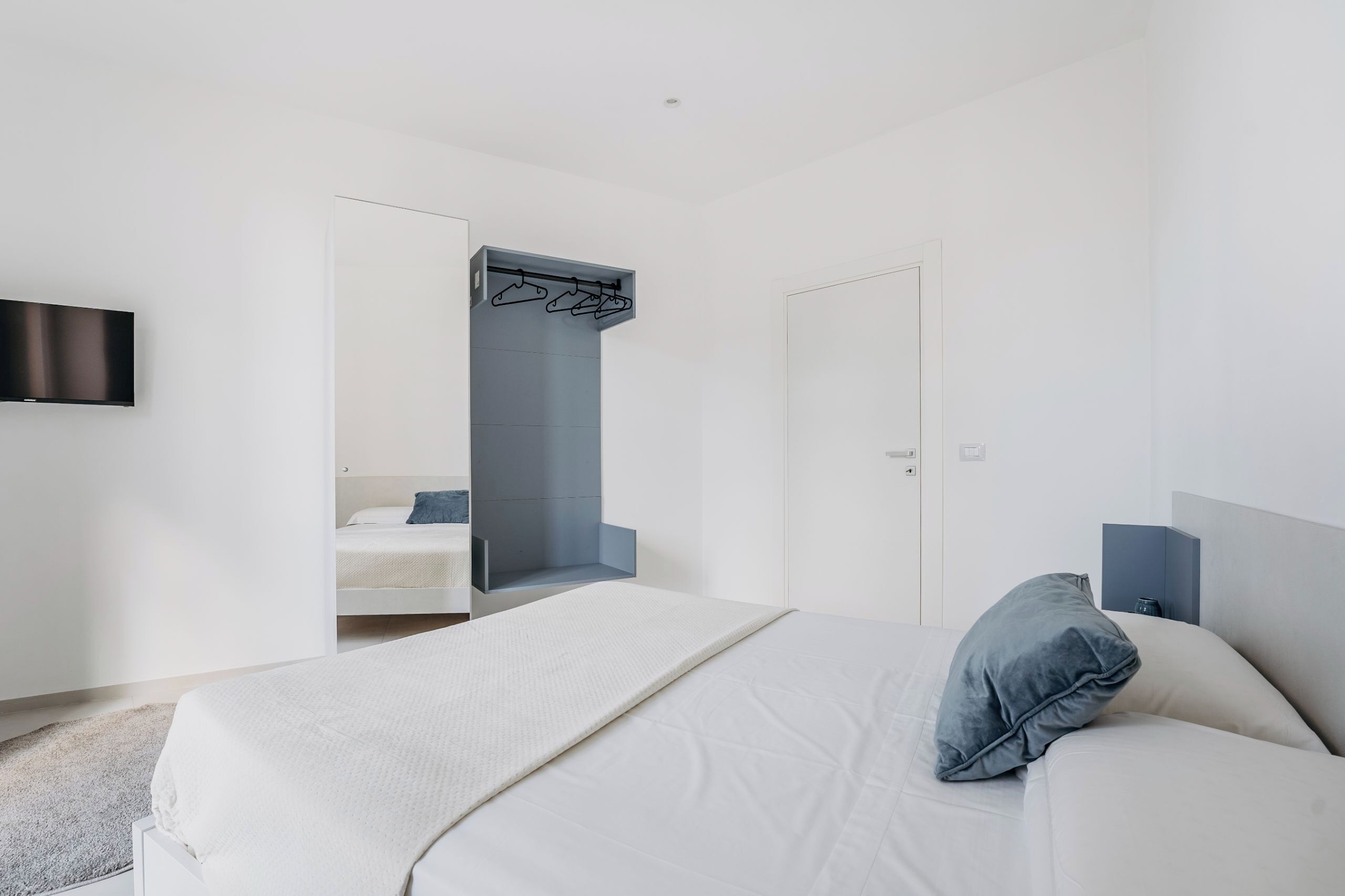 A modern hotel room with a bed, a TV mounted on the wall, and a built-in wardrobe with a mirror.